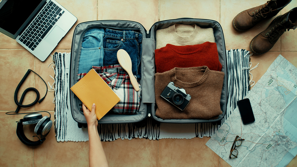 A person is packing a suitcase with clothes and a camera.