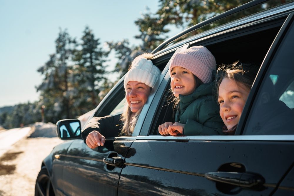 A woman and two children are looking out the window of a car.