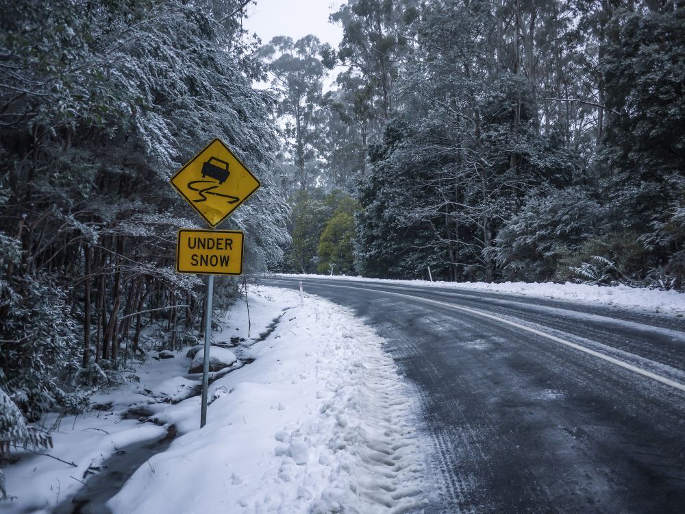 A yellow sign on the side of a snow covered road.