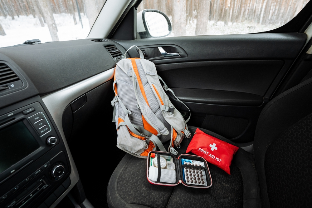 A backpack and first aid kit are in the back seat of a car.