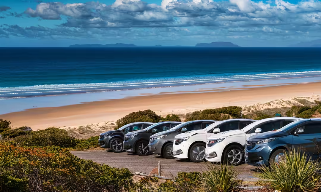A row of cars are parked next to a beach.