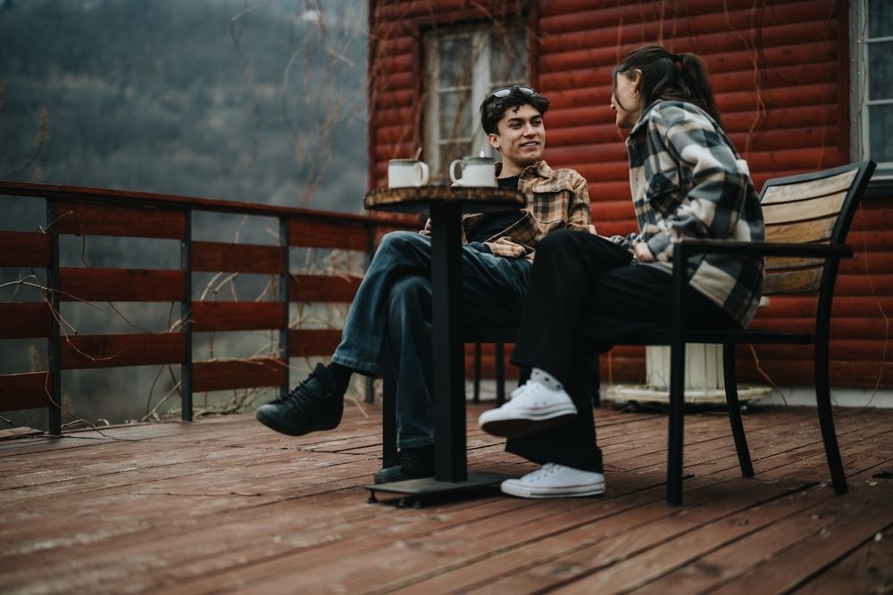 A man and a woman are sitting at a table on a deck.