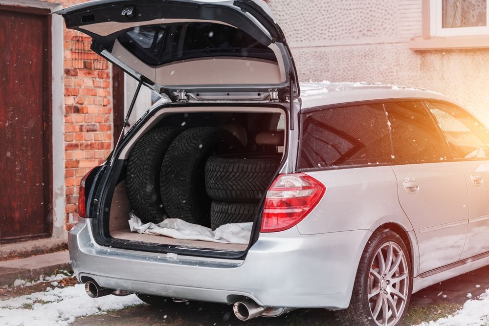 The trunk of a silver car is filled with tires.