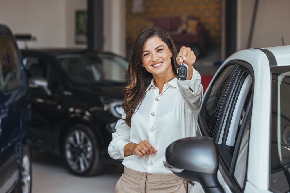 A woman is holding a car key in front of a car.