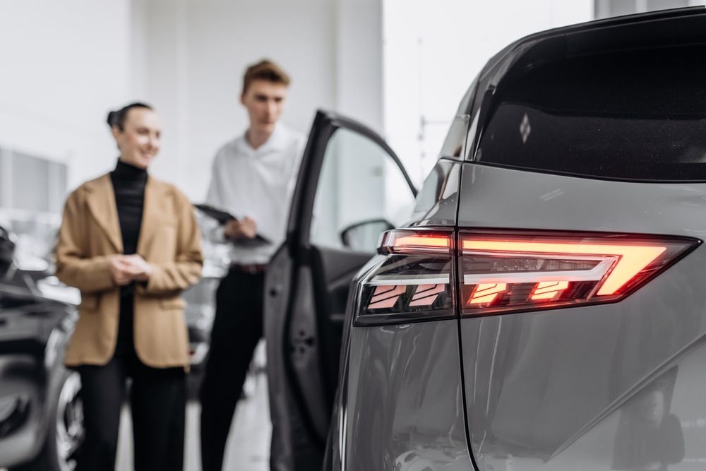 A man and a woman are looking at a car in a showroom.