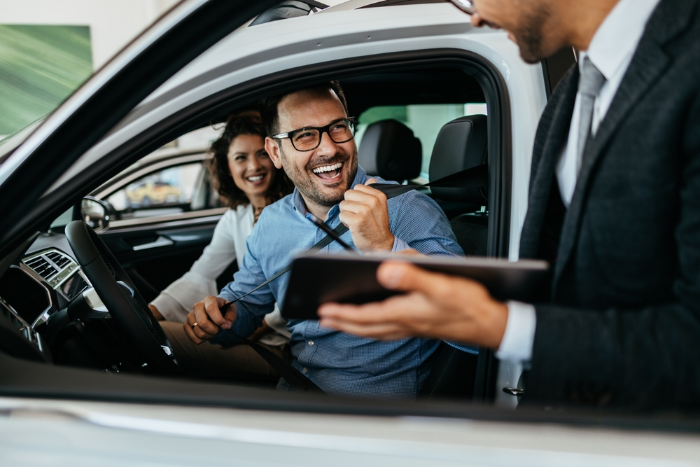 A man is holding a tablet while sitting in a car with a woman.