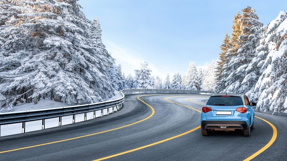 A blue car is driving down a snowy road.