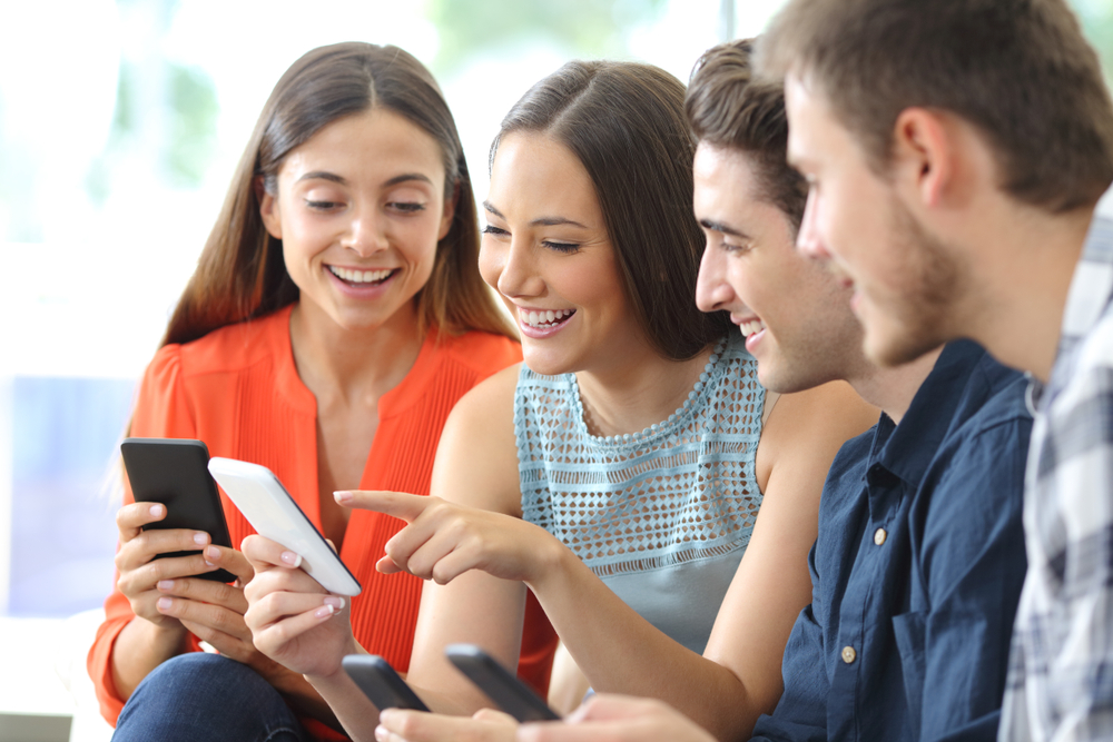 A group of people are sitting on a couch looking at their phones.