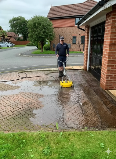 Person using a surface cleaner on a brick driveway, creating a wet area. Houses and a garage are visible.