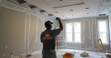 Man installing drywall on a ceiling in a room under construction, wearing a hat and work clothes.
