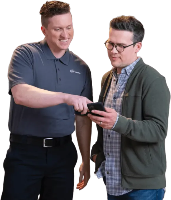 Two men are standing next to each other looking at a cell phone.