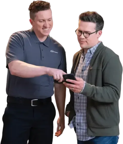 Two men are standing next to each other looking at a cell phone.