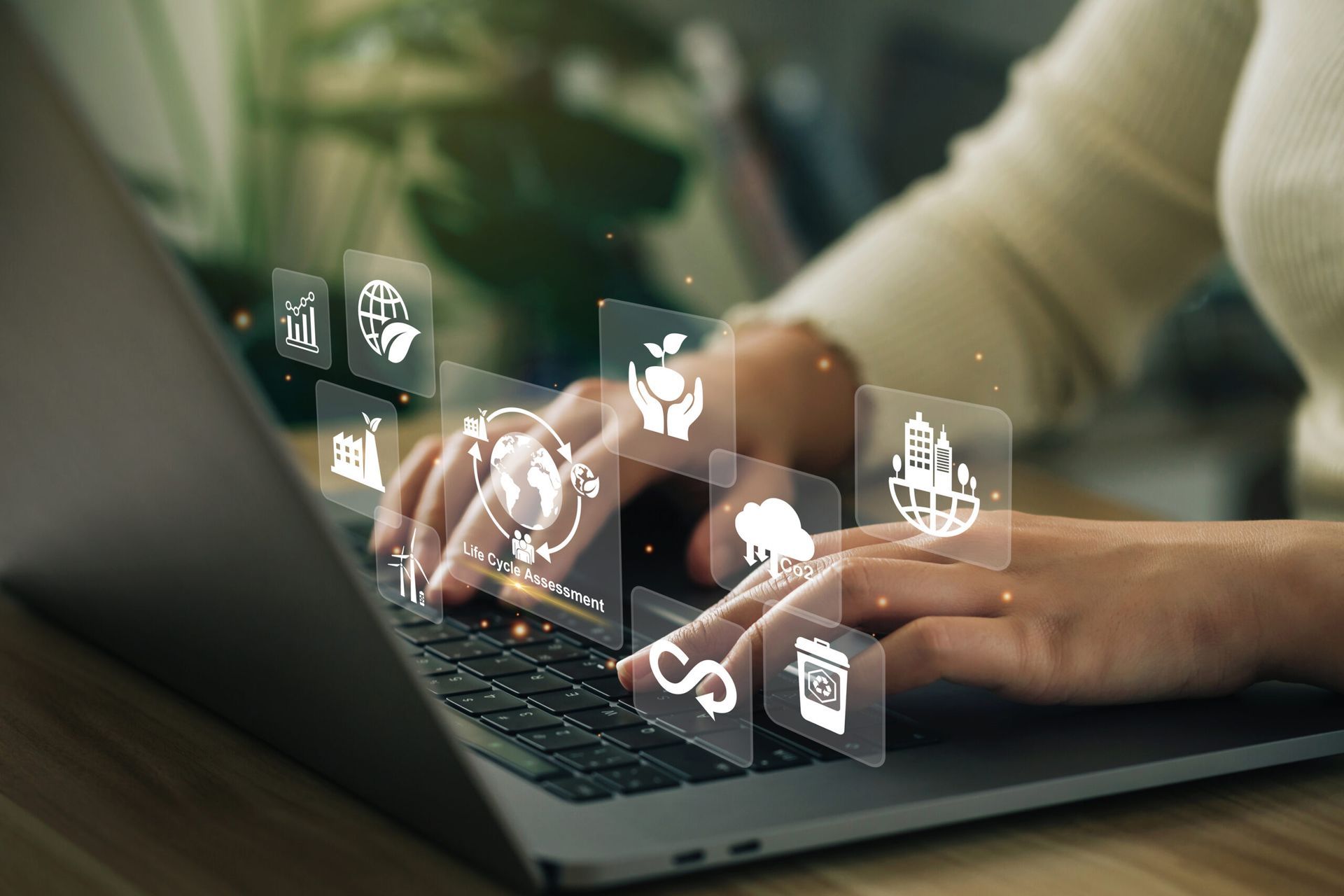 A person is typing on a laptop computer with icons coming out of the screen.