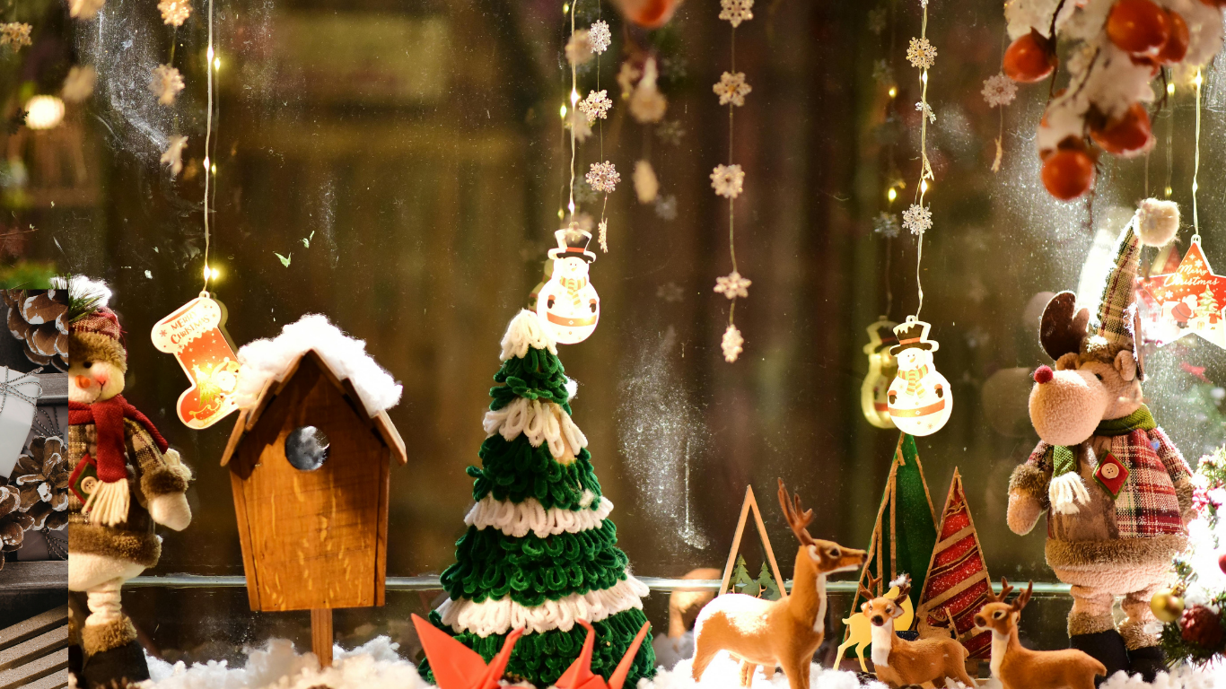 Christmas window display with festive ornaments, lights, and figurines on snowy surface.
