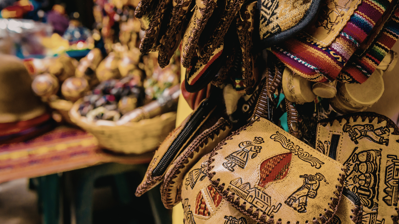Leather masks with intricate designs hang in a shop; a basket of goods is in the background.