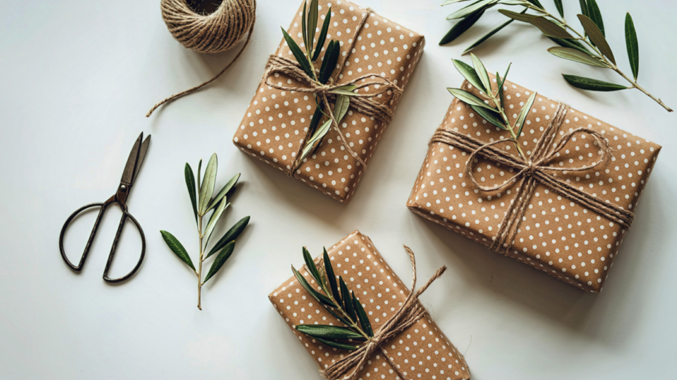 Brown polka dot wrapped gifts tied with twine and olive branches on a white surface with scissors and twine spool.