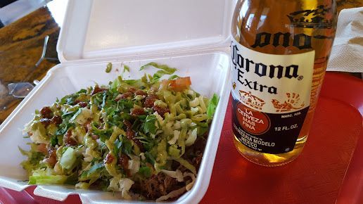 A bottle of corona extra beer next to a styrofoam container of food.