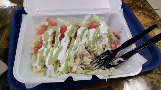 A styrofoam container filled with food and a fork on a blue tray.