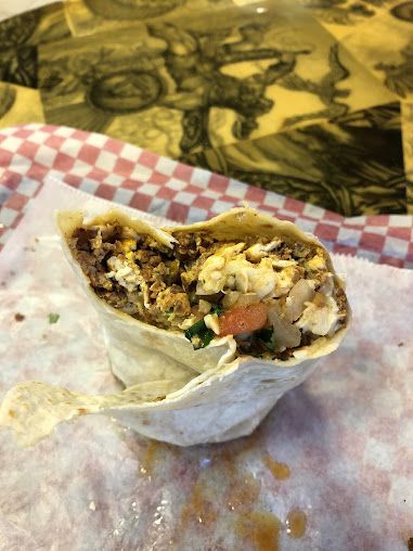 A burrito is cut in half on a checkered napkin on a table.