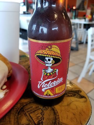 A bottle of victoria beer is sitting on a table next to a plate of food.