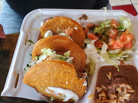 A styrofoam container filled with tacos , beans , lettuce and tomatoes.