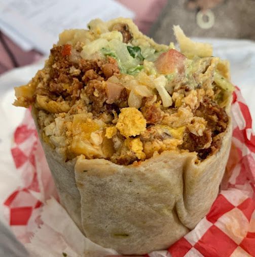 A burrito is sitting on a checkered napkin on a table.