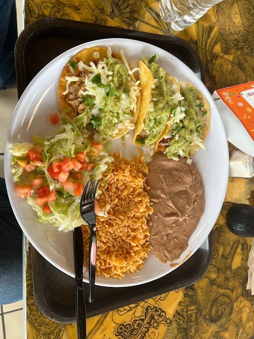A plate of mexican food with rice beans and tacos on a table.