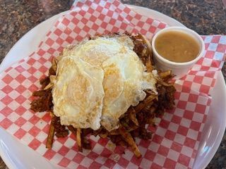 A plate of food with eggs , french fries and gravy on a checkered napkin.