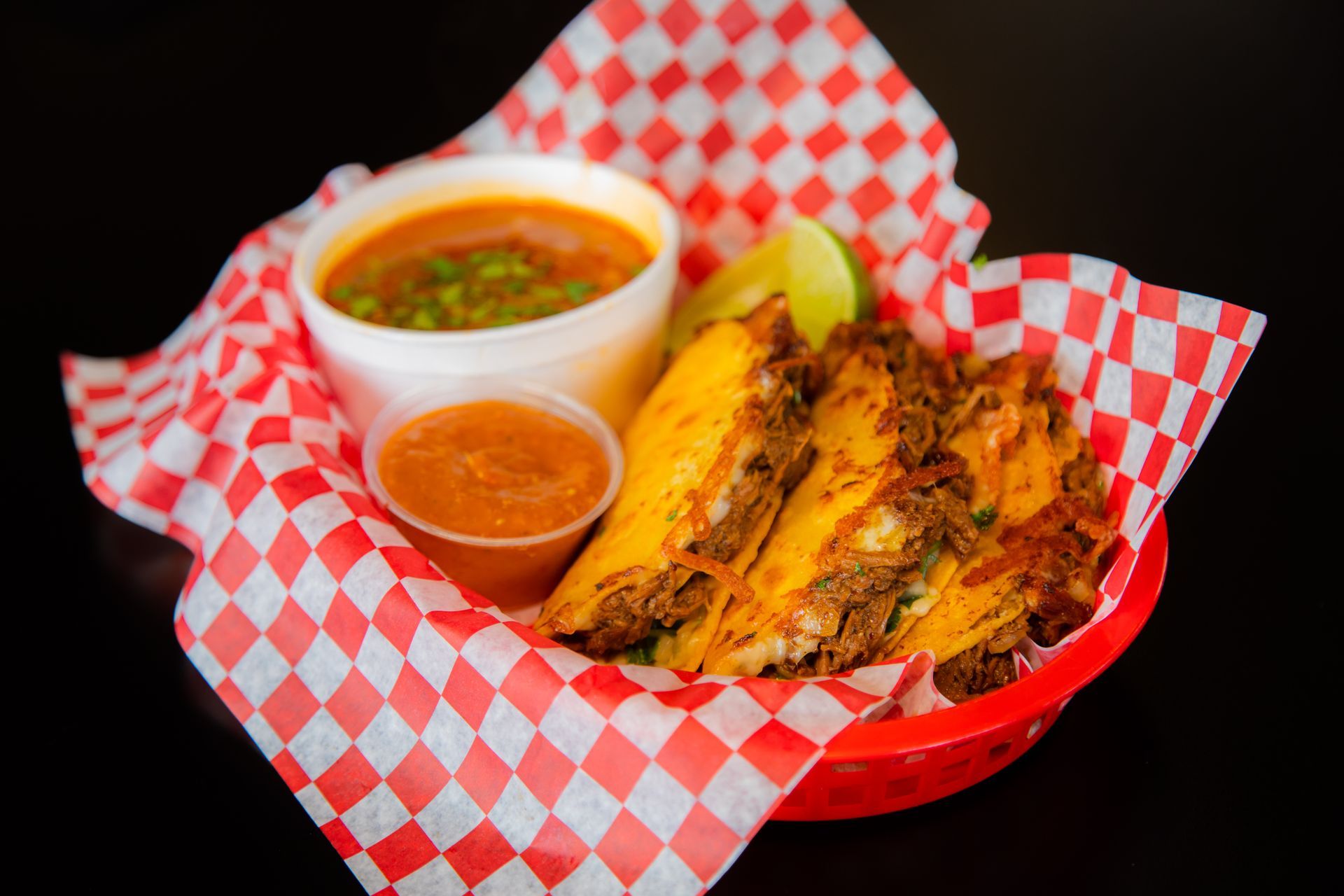 A basket of food with guacamole and salsa on checkered paper.