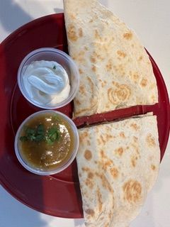 A quesadilla with sour cream and salsa on a red plate