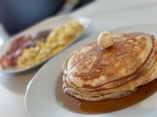 A stack of pancakes with syrup and butter on top on a plate.