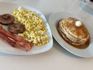 A plate of food with eggs , bacon , sausage and pancakes on a table.