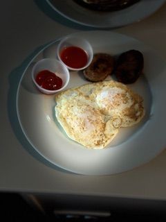A white plate topped with eggs sausage and ketchup