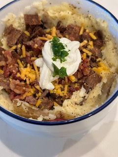 A bowl of mashed potatoes with bacon , cheese and sour cream on top.