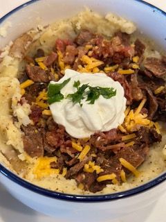 A bowl of mashed potatoes with meat , cheese , sour cream and bacon.