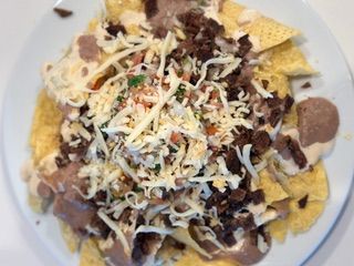 A white plate topped with nachos , beans , cheese and sauce.