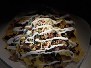 A close up of a plate of nachos with sour cream on top.