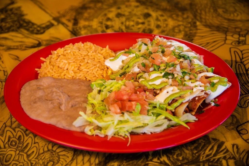 A red plate topped with rice , beans and enchiladas on a table.
