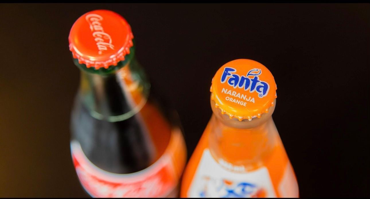 A bottle of coca cola and a bottle of fanta sit next to each other