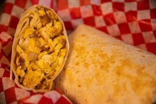 A burrito is cut in half and sitting on a checkered napkin.