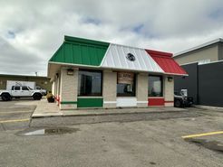 A small restaurant with a red , white and green roof is sitting in a parking lot.