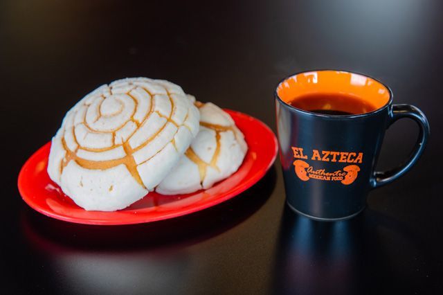 A cup that says el azteca on it next to a plate of food