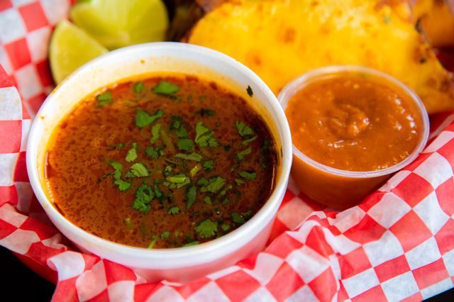 A bowl of soup and two cups of salsa are in a basket.