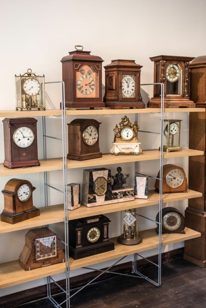 Shelves displaying a collection of various antique clocks with wooden and glass cases.