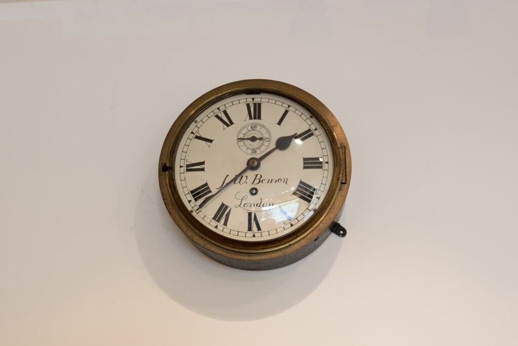 Antique wall clock with Roman numerals, brass bezel, and black hands on a white background.
