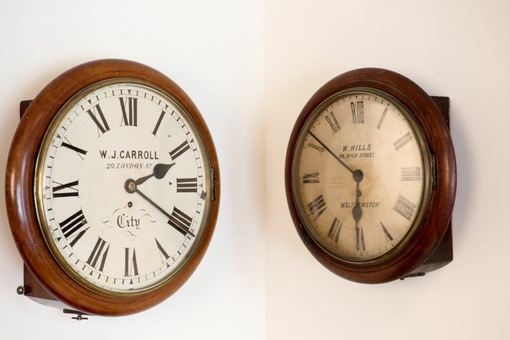 Two antique wooden wall clocks side by side with Roman numerals and visible clock hands.