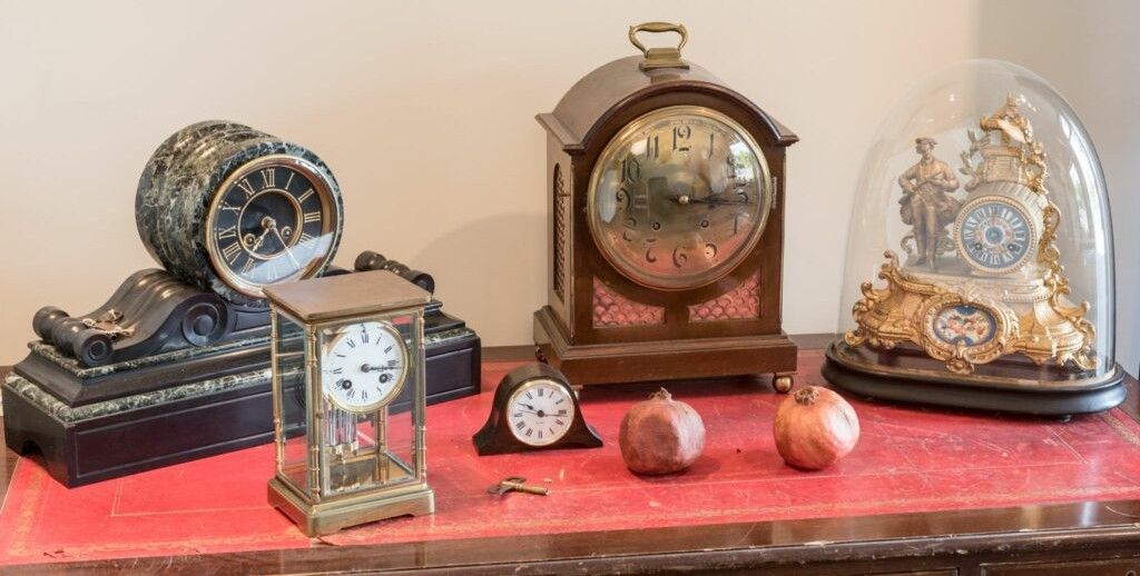 Collection of antique clocks displayed on a red surface, some with glass domes.