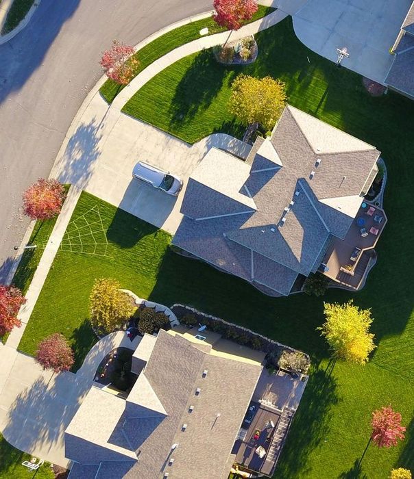 Aerial view of houses with green lawns and autumn trees along a curved road.
