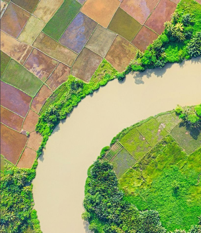 Aerial view of colorful fields divided by a winding river, with patches of green vegetation along the banks.
