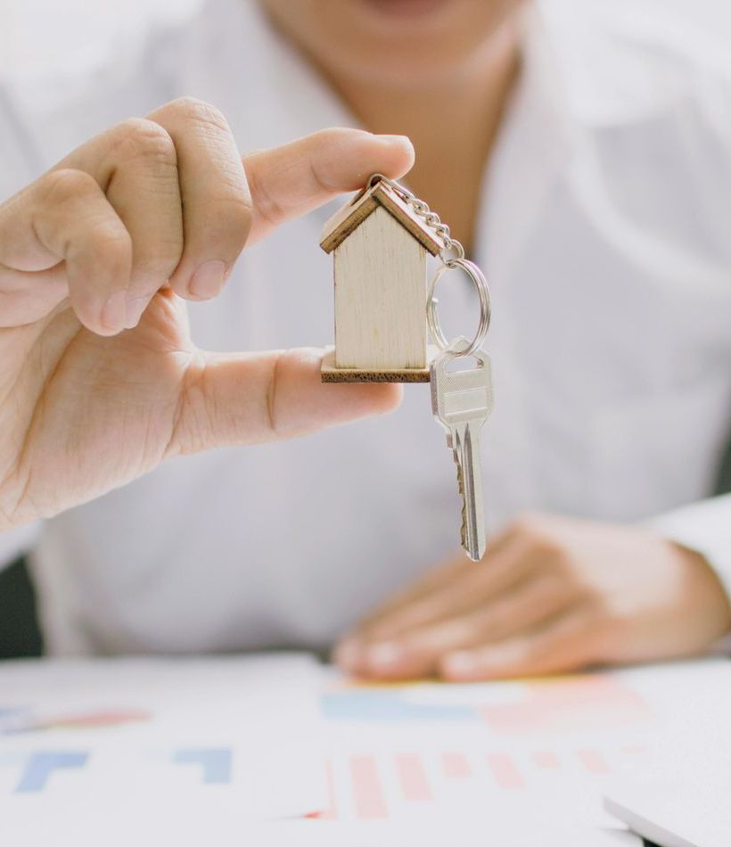 Person holding a house-shaped keychain with keys above colorful charts, possibly about real estate.